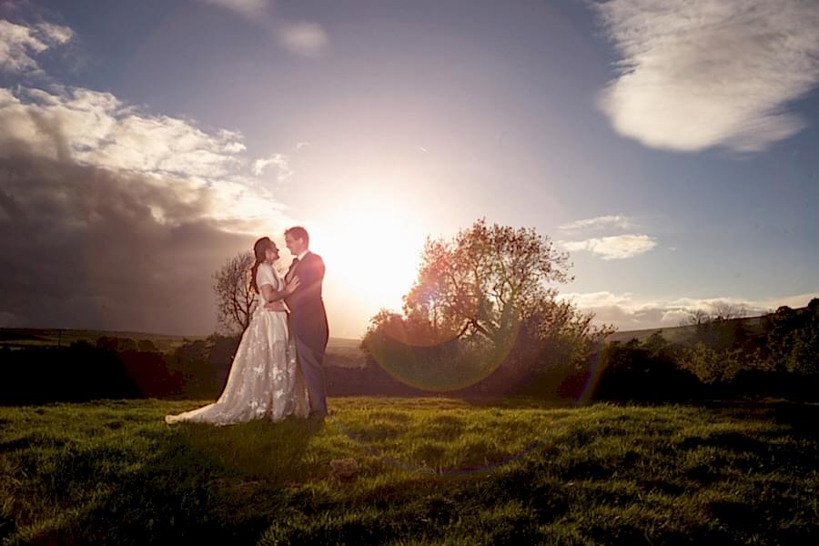 A couple embracing in a sunlit field at sunset captured by a North East Wedding Photographer.